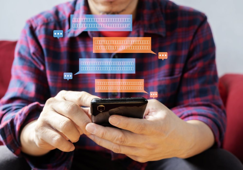 Glad fashionable young bearded guy wears stylish clothes and denim shirt, has trendy hairstyle, happy to exchange messages with friends, uses free internet connection on electronic modern gadget