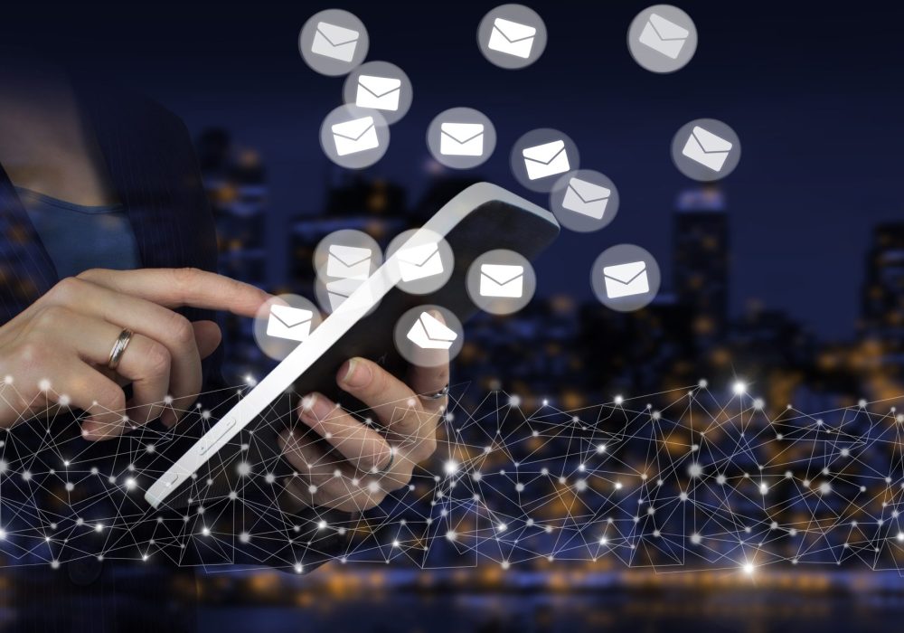 Sending email.Bulk mail. Hand touch white tablet with digital hologram Email and sms sign on city dark blurred background. Business email concept